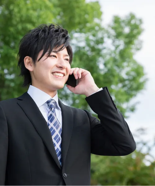 屋外で笑顔でスマートフォンを使って電話対応をするスーツ姿の男性